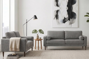 Configuración moderna de sala con sofá gris de dos plazas, loveseat a juego con manta beige, mesita auxiliar de madera, lámpara de pie negra, alfombra y planta.