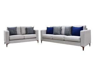 Sofás y loveseat grises con cojines azules y estampados sobre fondo blanco.