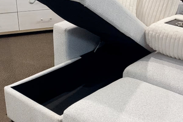 Sofá modular contemporáneo tapizado en tela blanca texturizada con compartimento de almacenamiento oculto bajo el asiento elevable, cojines acanalados en color crema y consola central con portavasos integrados.