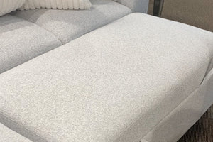 Vista cercana de un sofá modular tapizado en tela blanca texturizada con extensión tipo chaise longue acolchada, diseñada para brindar mayor espacio y comodidad al recostarse.