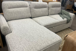 Primer plano de sofá seccional con chaise en tela color marfil jaspeado, respaldos altos acolchados y brazos redondeados. Incluye manta decorativa sobre el asiento y diseño contemporáneo orientado al confort y almacenamiento oculto.