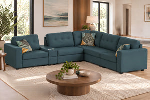 Sofá seccional en forma de L, tapizado en tela azul petróleo, con respaldos acolchados, brazos rectos, cojines decorativos y portavasos integrados. Ubicado en sala moderna con mesa de centro redonda de madera.