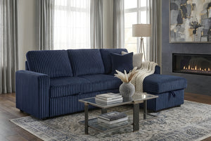 Sofá seccional reversible tapizado en tela acanalada azul marino, con chaise longue integrada y cojines decorativos. Se muestra en una sala moderna junto a una mesa de centro de vidrio, alfombra y chimenea.