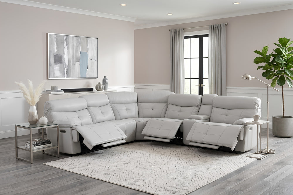 Un gran sofá modular de color gris claro con múltiples asientos reclinables y reposapiés extensibles, mostrado unas mesas auxiliares y una planta en maceta.