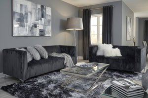 Sala de estar moderna con sofá y loveseats gris oscuro, una mesa de centro de cristal y arte abstracto en una pared gris.