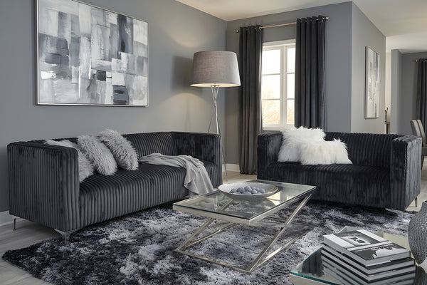 Sala de estar moderna con sofá y loveseats gris oscuro, una mesa de centro de cristal y arte abstracto en una pared gris.
