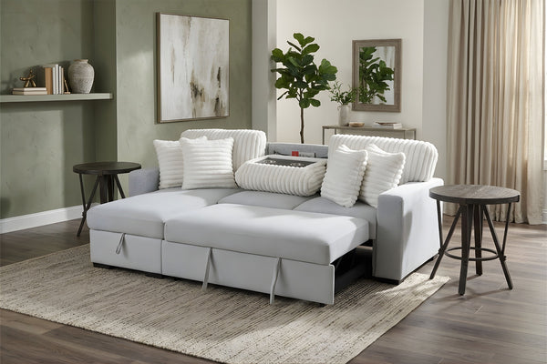 Sofá modular contemporáneo tapizado en tela blanca, con asientos amplios, cojines decorativos acanalados y chaise longue integrada, acompañado de mesas auxiliares negras en una sala moderna y luminosa.