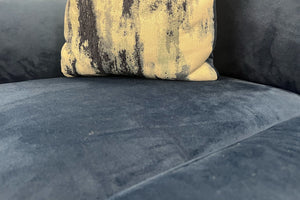 Primer plano de asiento en terciopelo azul marino con cojín decorativo estampado en tonos crema y azul, resaltando la textura suave y acolchada del sofá moderno.