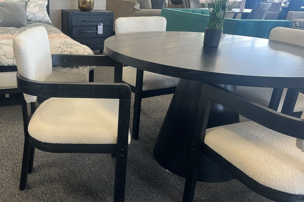 Mesa redonda de comedor hecha de madera negra con base cilíndrica y con cuatro sillas. 