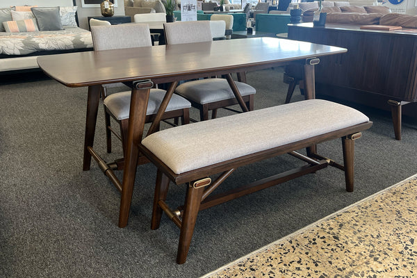 Juego de comedor contemporáneo con mesa rectangular de madera oscura, dos sillas tapizadas en tela beige y banco acolchado a juego. Exhibido en una sala de muebles, destacando líneas modernas, acabados cálidos y diseño funcional.