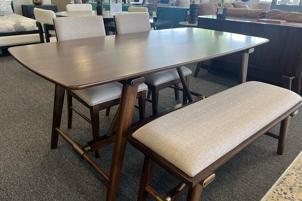 Juego de comedor contemporáneo con mesa rectangular de madera oscura, dos sillas y banco tapizados en tela beige. Presentado en una sala de exhibición, destacando su diseño moderno, estructura robusta y acabados en tonos cálidos.