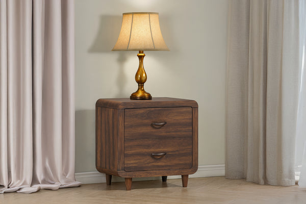 Mesita de noche de madera con lámpara sobre un fondo de cortina neutra.