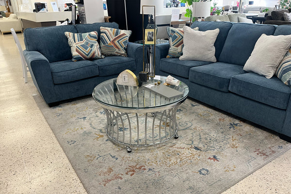 Sofá azul con cojines estampados y una mesa de centro de cristal en un salón.