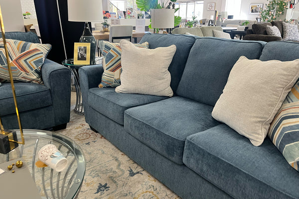 Sofá azul con cojines decorativos en un ambiente de sala de exposición