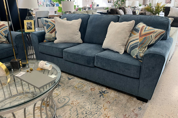 Sofá azul con cojines estampados y lisos en un ambiente de sala de exposición