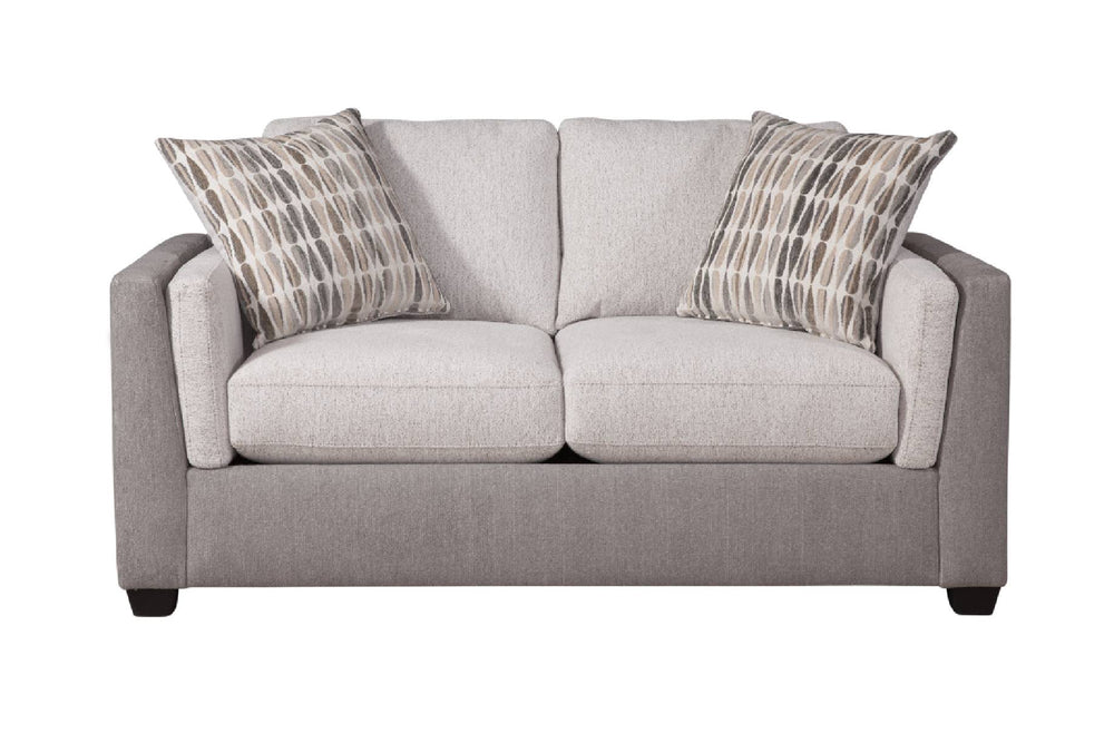 Loveseat de dos plazas tapizado en tela color beige claro, con cojines de asiento y respaldo acolchados y apoyabrazos redondeados. Incluye dos cojines decorativos con patrón en tonos neutros. El sofá presenta patas bajas oscuras y diseño contemporáneo, mostrado sobre fondo blanco.