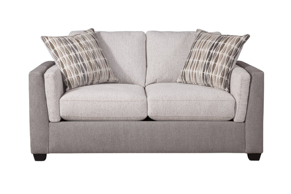 Loveseat de dos plazas tapizado en tela color beige claro, con cojines de asiento y respaldo acolchados y apoyabrazos redondeados. Incluye dos cojines decorativos con patrón en tonos neutros. El sofá presenta patas bajas oscuras y diseño contemporáneo, mostrado sobre fondo blanco.