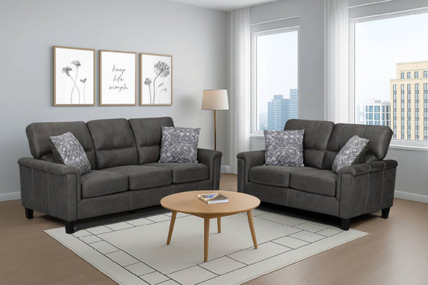 Un conjunto de sala de estar de tela gris oscuro que incluye un loveseat y un sofá con cojines decorativos estampados a juego, dispuestos en una sala de estar moderna con una mesa de centro redonda de madera, una alfombra blanca y una lámpara de pie.