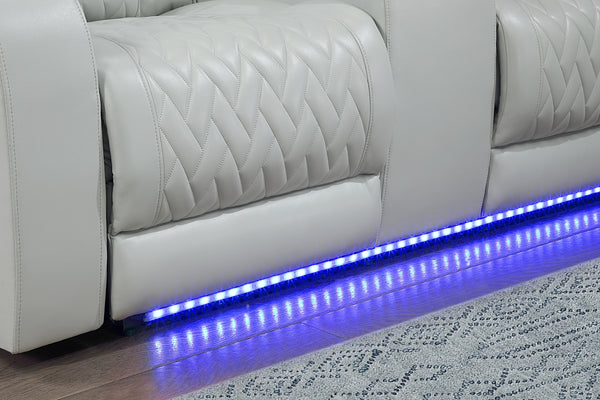 Primer plano del tapizado acolchado en color gris claro de un sofá reclinable, con patrón geométrico cosido y tira de iluminación LED azul integrada en la base, que aporta un detalle moderno y decorativo.