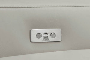 Primer plano de un panel de toma de corriente de metal plateado con dos puertos USB-C y dos terminales de tornillo, montado sobre una superficie de cuero beige claro.