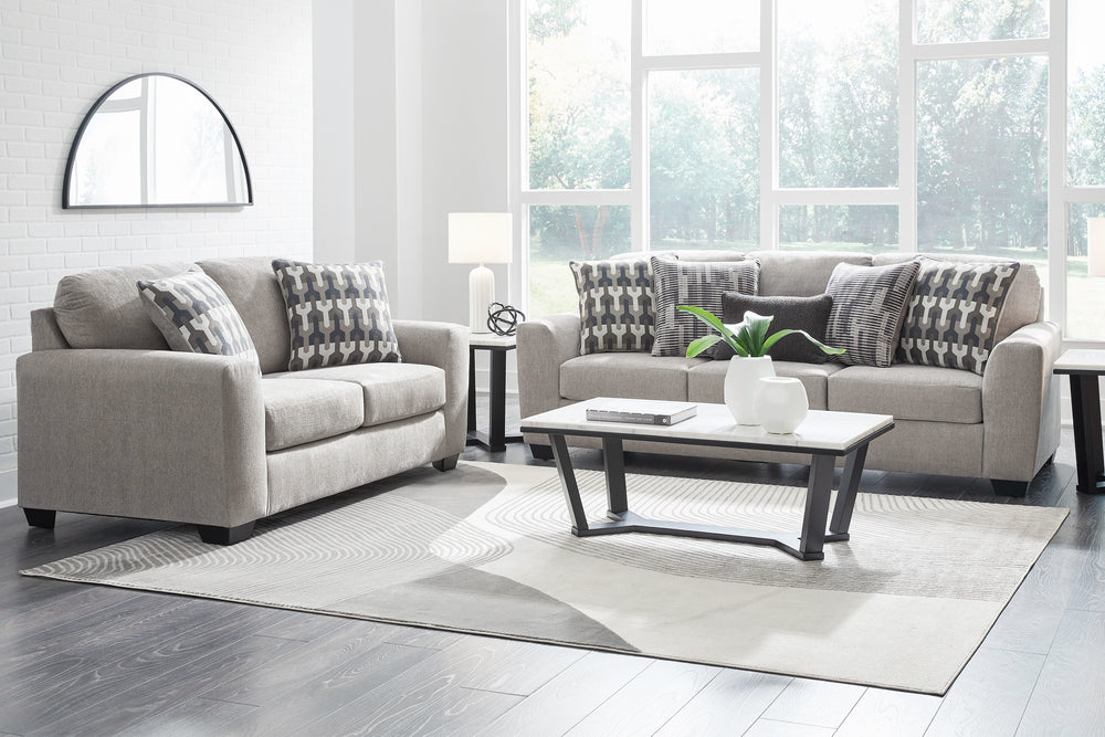 Sofá y loveseat de color gris claro con cojines sobre su fondo blanco. 
