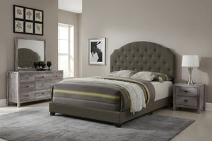 Cama tapizada en gris en un entorno de dormitorio con gavetero con espejo y lámpara encima de una mesa de noche. 