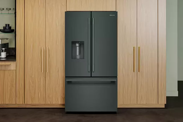 Una nevera de doble puerta de color verde con una gaveta congeladora en la parte inferior se sitúa en el centro entre los armarios de cocina de madera clara.