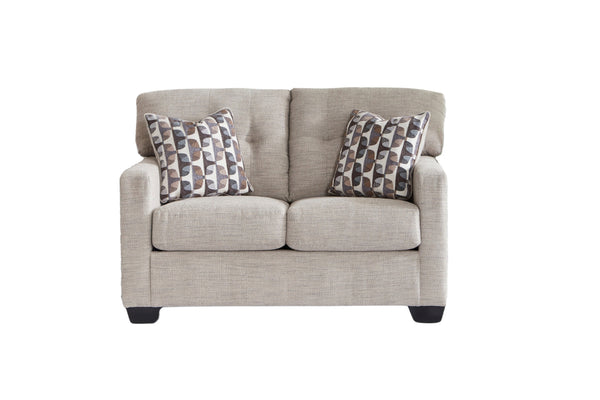 Loveseat de color beige con cojines decorativos sobre un fondo blanco. 