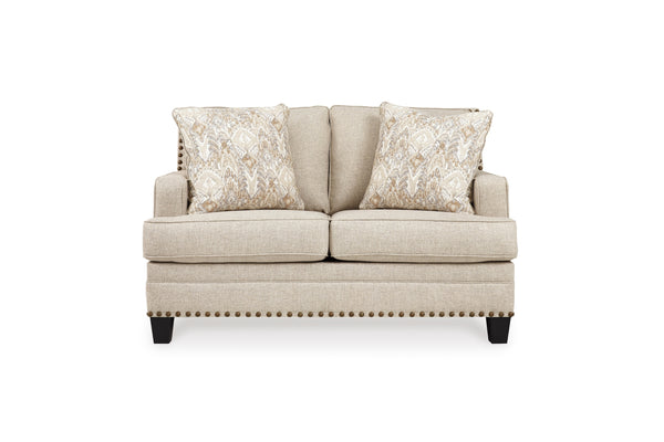 Loveseat de color crema con cojines decorativos sobre un fondo blanco. 