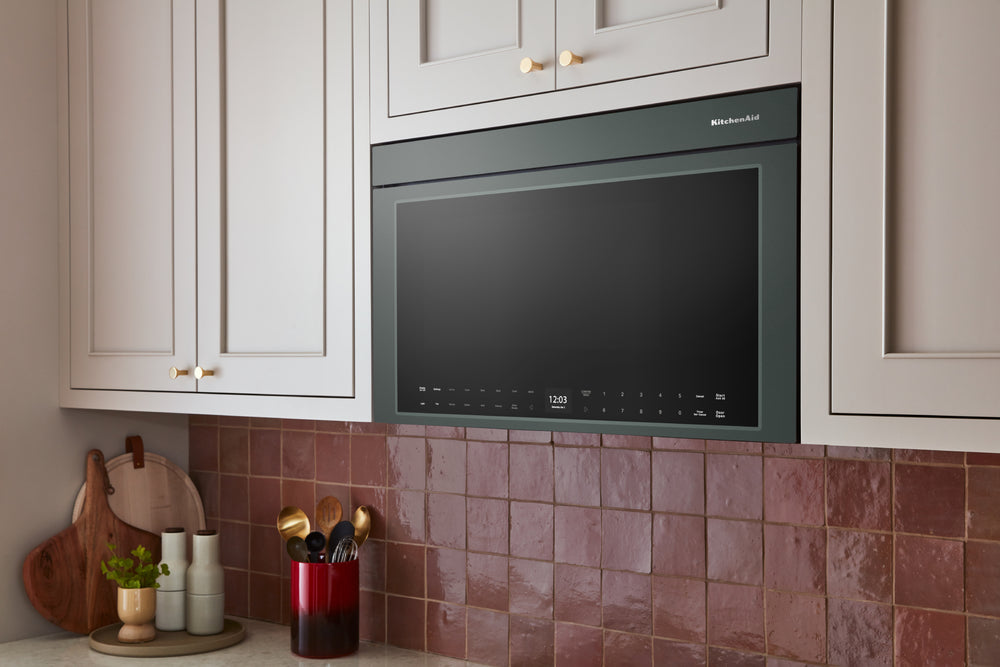 Un microondas KitchenAid para instalar sobre la encimera, con acabado en verde, puerta de cristal negro y panel de control digital en la parte inferior.
