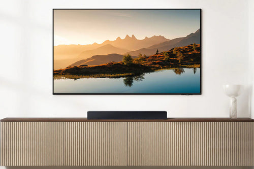 Televisor que muestra un paisaje escénico con montañas y un lago, montado en una pared blanca.