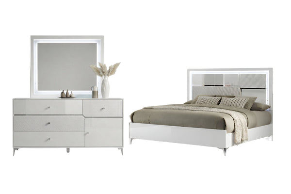 Un moderno conjunto de muebles de dormitorio que incluye un gavetero blanco de seis gavetas con espejo rectangular incorporado y una cama blanca a juego con cabecero geométrico, todo ello decorado con ropa de cama beige sobre un fondo blanco liso.