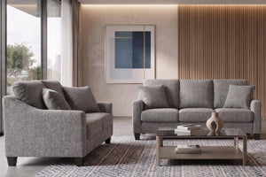 Sala moderna con un loveseat gris a la izquierda y un sofá de tres plazas a la derecha, en torno a una mesa de centro de vidrio sobre una alfombra. El fondo tiene una pared beige con arte abstracto, paneles de madera y un ventanal.