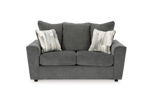 Loveseat gris con cojines decorativas sobre un fondo blanco. 