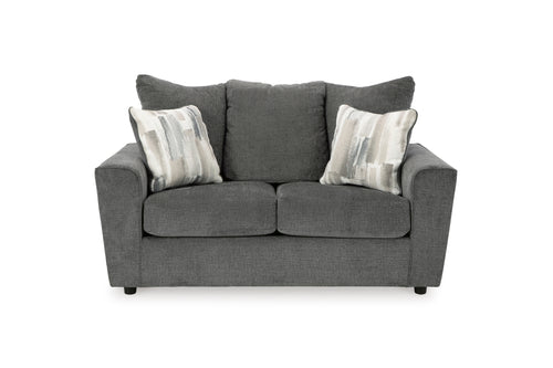 Loveseat gris con cojines decorativas sobre un fondo blanco. 
