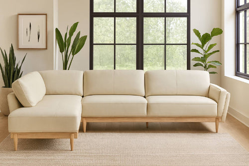 Sofá chaise de color beige en una sala neutral con plantas decorativas. 