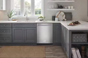 Un lavaplatos empotrado de acero inoxidable instalado en una cocina moderna con armarios gris oscuro, encimeras blancas y una ventana detrás.