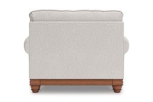 Vista posterior de silla de acento de color beige con brazos y un cojín decorativo sobre un fondo blanco. 