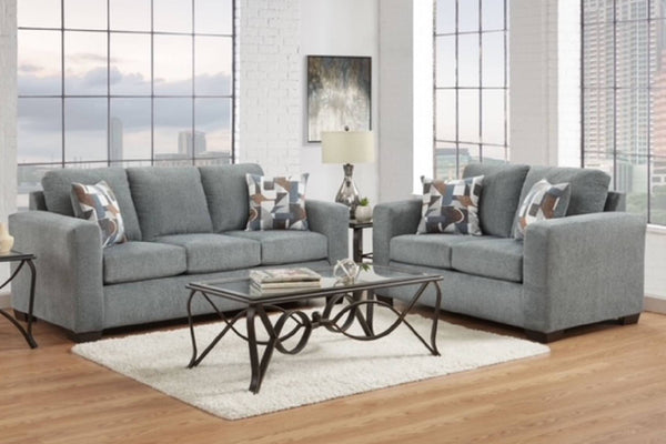 Sofá y loveseat de color gris con elementos decorativos y una mesa de centro en una sala de hogar con ventanas. 