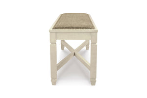 Un banco de madera blanca con un cojín de asiento tejido de color beige, mostrado desde un ángulo frontal de tres cuartos sobre un fondo blanco.