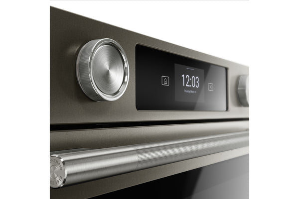 Primer plano del panel de control de un horno empotrado con un dial de metal cepillado, una pantalla digital negra que muestra las 12:03 y un tirador de acero inoxidable sobre un fondo blanco.