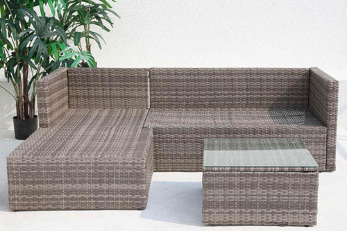 Conjunto de muebles de exterior de ratán sin cojines con una mesita con tope de cristal sobre un fondo de patio.