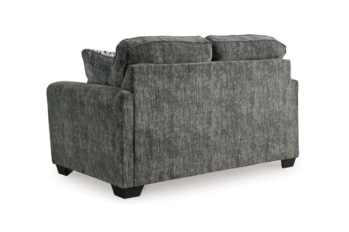 Vista posterior de loveseat de color gris oscuro con cojines decorativos sobre un fondo blanco. 