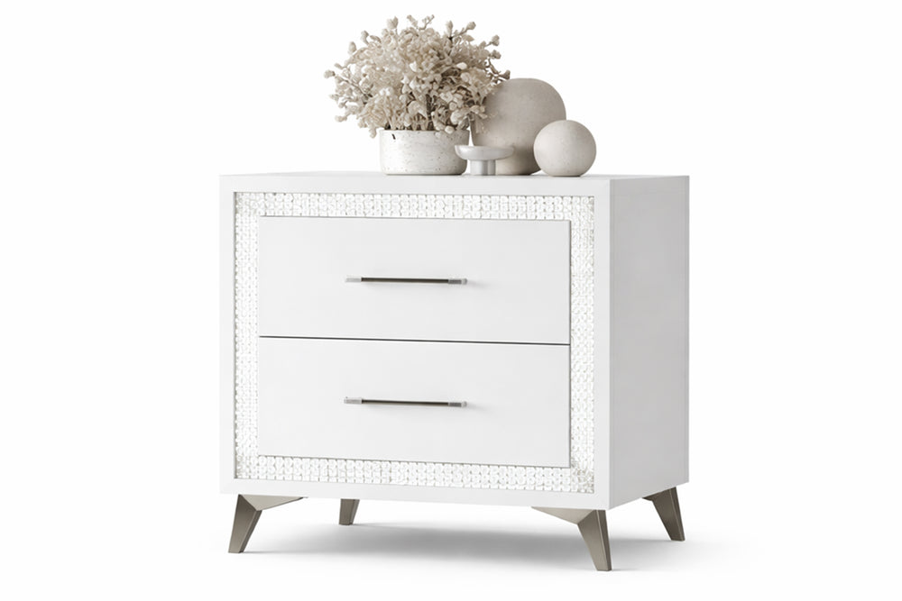 Mesa de noche blanco con dos gavetas con objetos decorativos sobre un fondo blanco. 