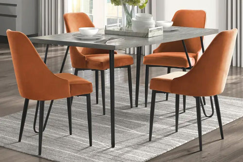 Mesa rectangular con patas acabadas en negro, tope de madera marrón, y cuatro sillas de color anaranjado con respaldar en una sala moderna. 