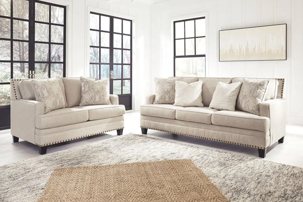 Sofá y loveseat de color crema con cojines decorativos sobre un fondo blanco. 