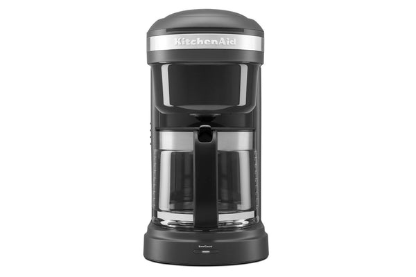 Cafetera KitchenAid en gris oscuro y negro con jarra de cristal transparente, mostrada sobre un fondo blanco liso.