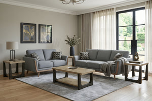 Una sala de estar moderna que cuenta con un juego de sofás de tela gris claro con estructura de madera oscura, decorado con cojines estampados, una alfombra gris a juego, una mesa de centro de madera y mesas auxiliares.