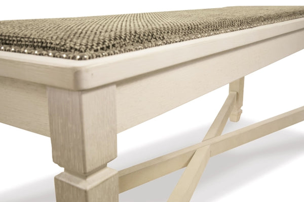 Primer plano de un banco con estructura de madera pintada en color crema claro y cojín de asiento tejido con textura en tonos beige y marrón.