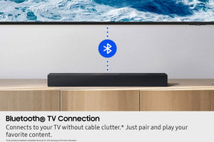 Barra de sonido con icono de Bluetooth sobre una superficie de madera, TV de fondo que muestra vista al mar.